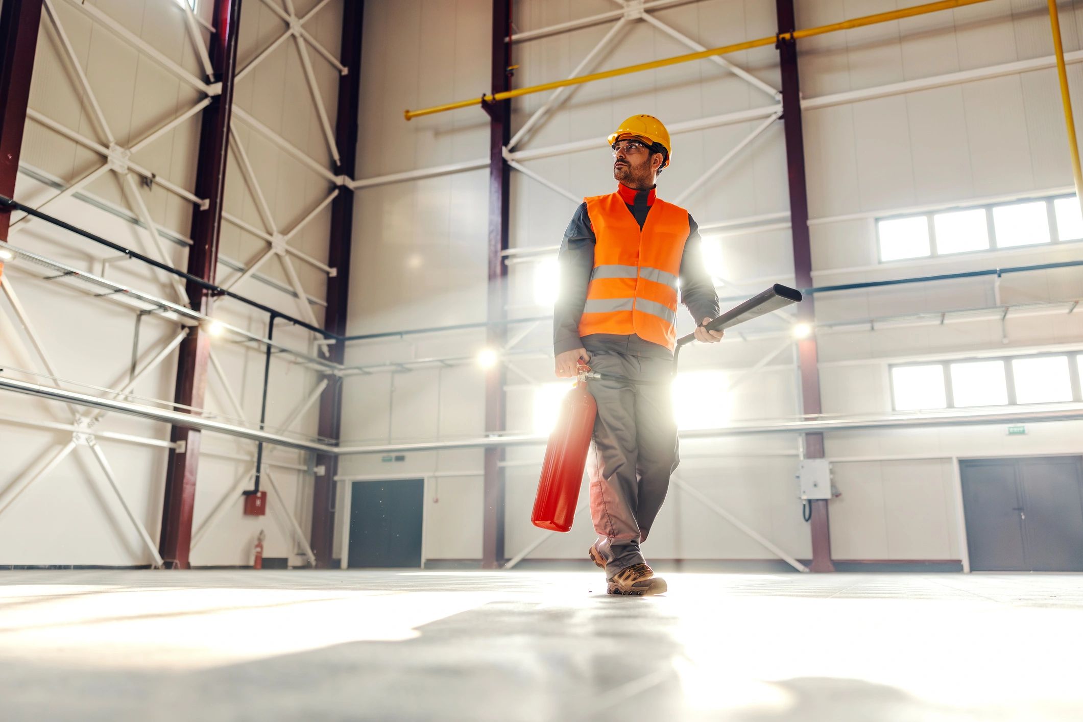 Worker carrying a fire extinguisher in an industrial warehouse